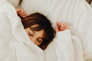 A woman with brown hair is sleeping on a bed with white bed linen.
