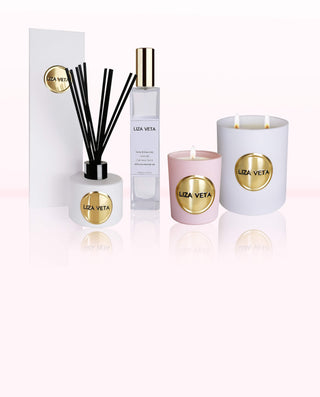 On pink background there are one pink votive candle, one white reed diffuser and one large white candle.