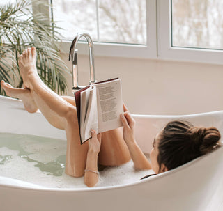 A woman is taking a bath, relaxing and unwinding while reading a book.