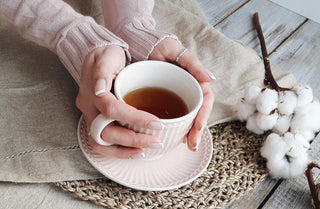 A woman's hands holding a white teacup filled with black tea, with steam rising from the cup.