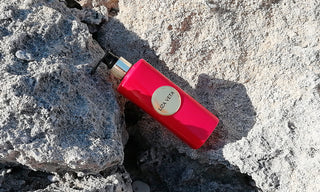 A vibrant red bottle of Neroli hand and body lotion resting on a textured surface.