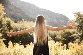 Amidst the rolling hills of a picturesque countryside, a blonde woman with flowing locks stands with arms outstretched, basking in the warm glow of the sun.