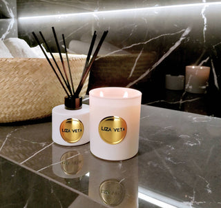 Aromatherapy reed diffuser and natural candle in white glass are on the table