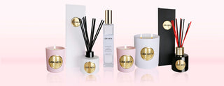 On pink background there are two pink votive candles, one white reed diffuser, one large white candle, one room and linen spray and one black reed diffuser.
